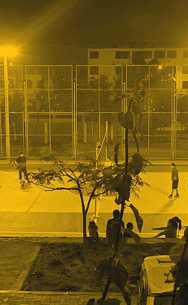 La losa deportiva iluminada de noche con la red de vóley armada, en tonos amarillos